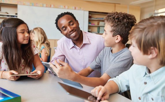 A black male educator speaks with a multiracial group of young students in his classroom