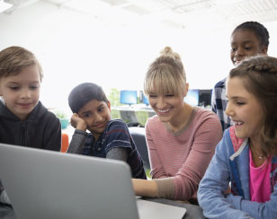 A white woman educator works with a multiracial group of students at a laptop